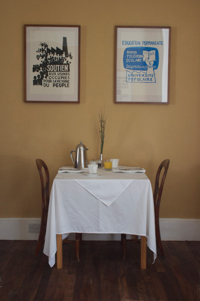 Breakfast Table laid with stainless steel coffee pat, juices and prints on the wall above.